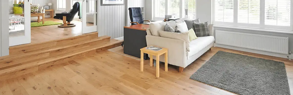 A modern living room with professionally installed laminate flooring, a beige sofa, a small side table, a gray rug, and large windows with white shutters in Boulder, CO